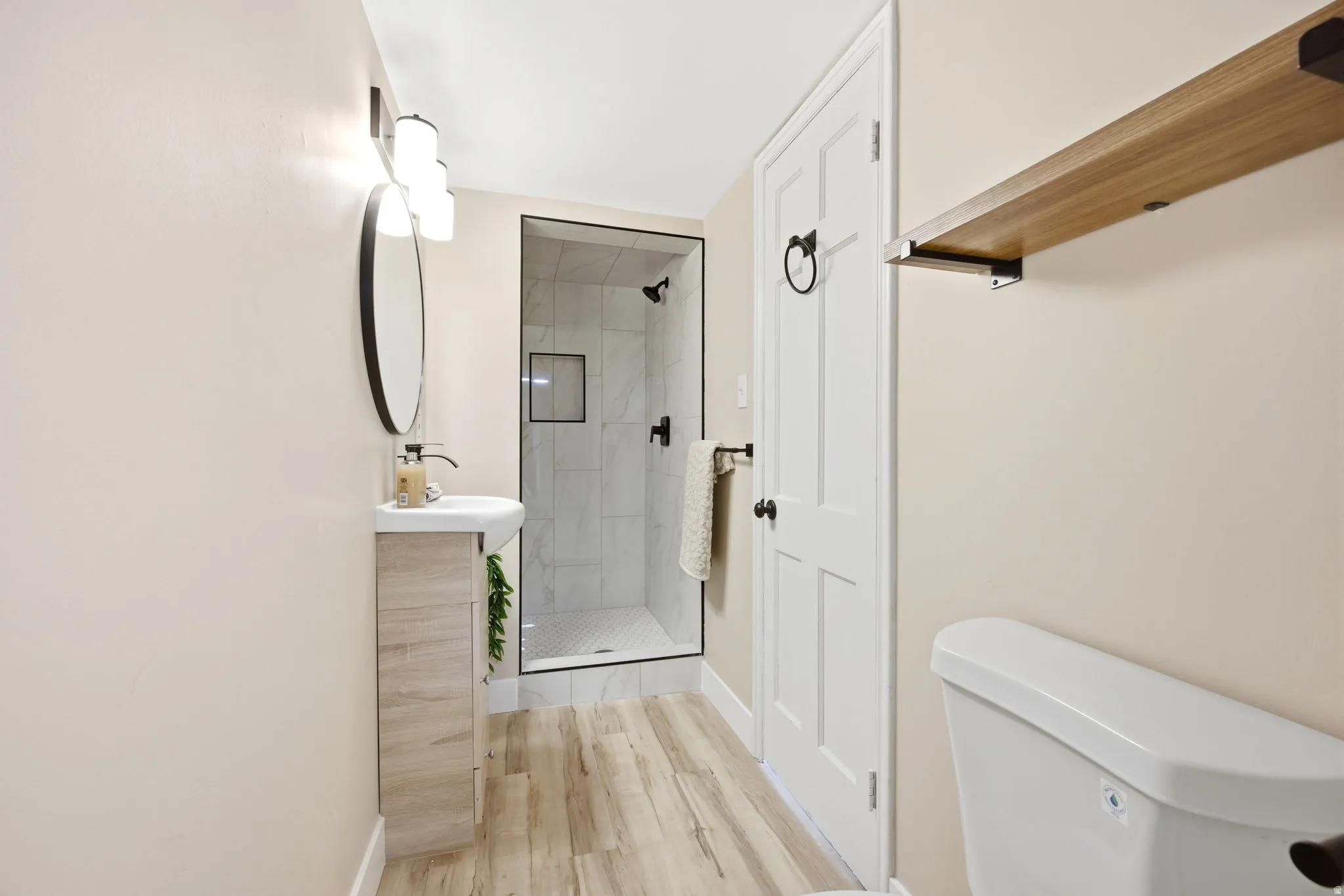 Bathroom featuring a walk-in shower with black frame, wood-finish flooring, and a pedestal sink with vanity