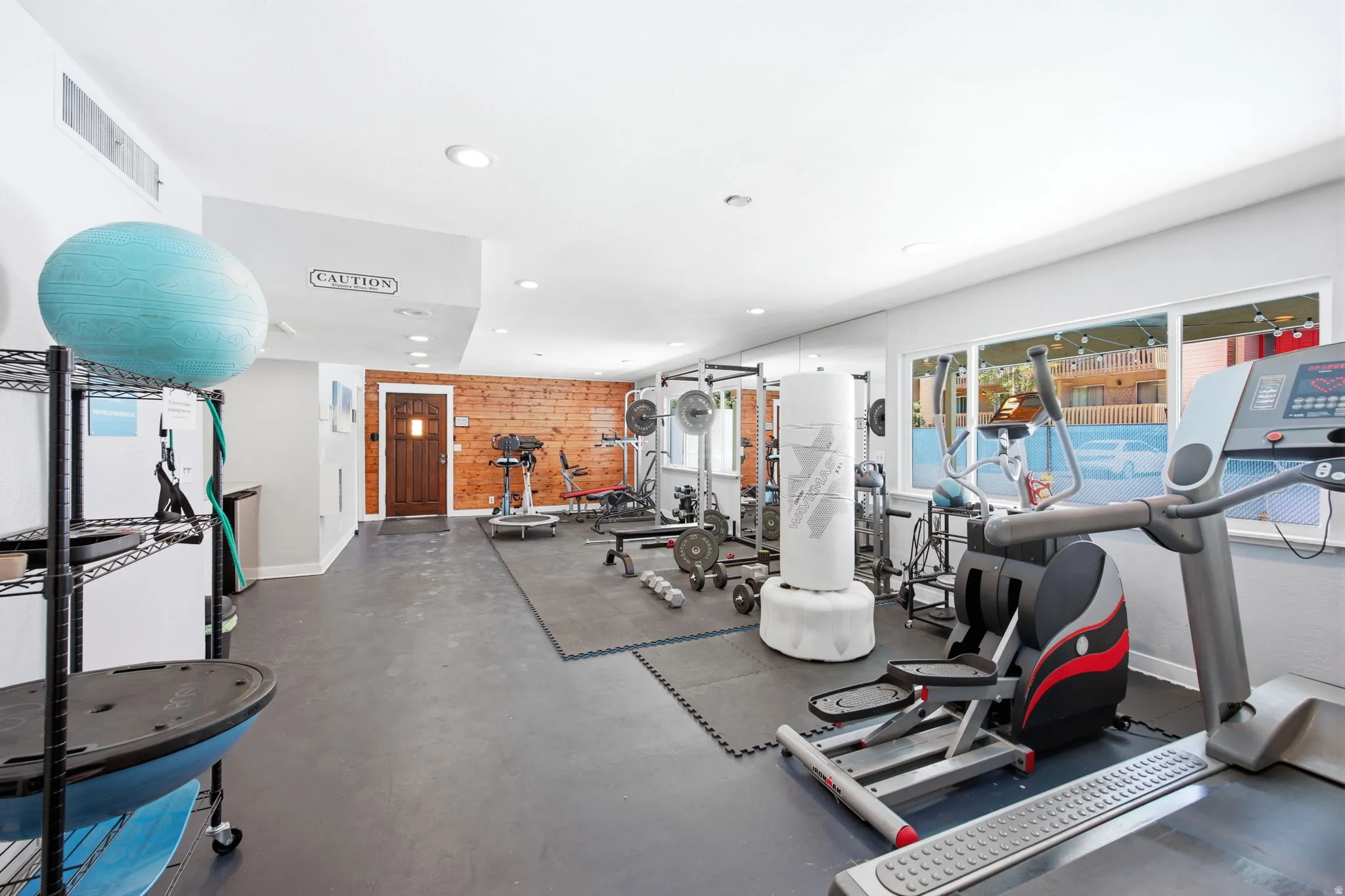 Spacious recreational room featuring rubber flooring, recessed lighting, and a prominent window line