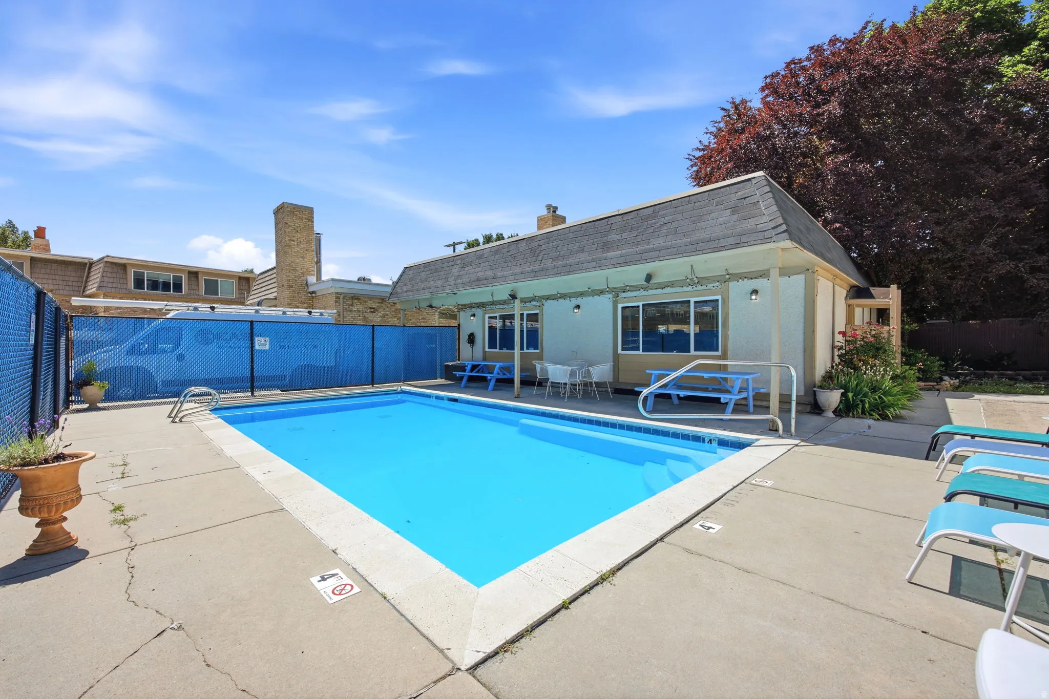Outdoor swimming pool with concrete surround, fenced perimeter, and nearby amenity building featuring a covered patio