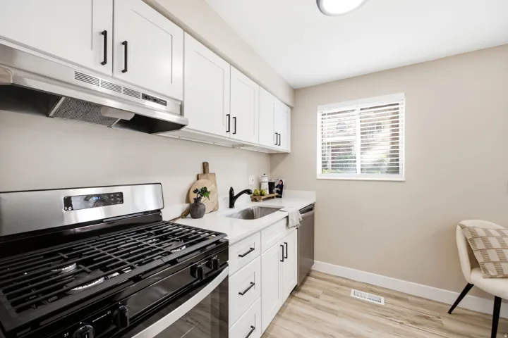 Kitchen featuring white cabinetry, a stainless steel range hood, a black gas range, white countertops, and wood-finish flooring