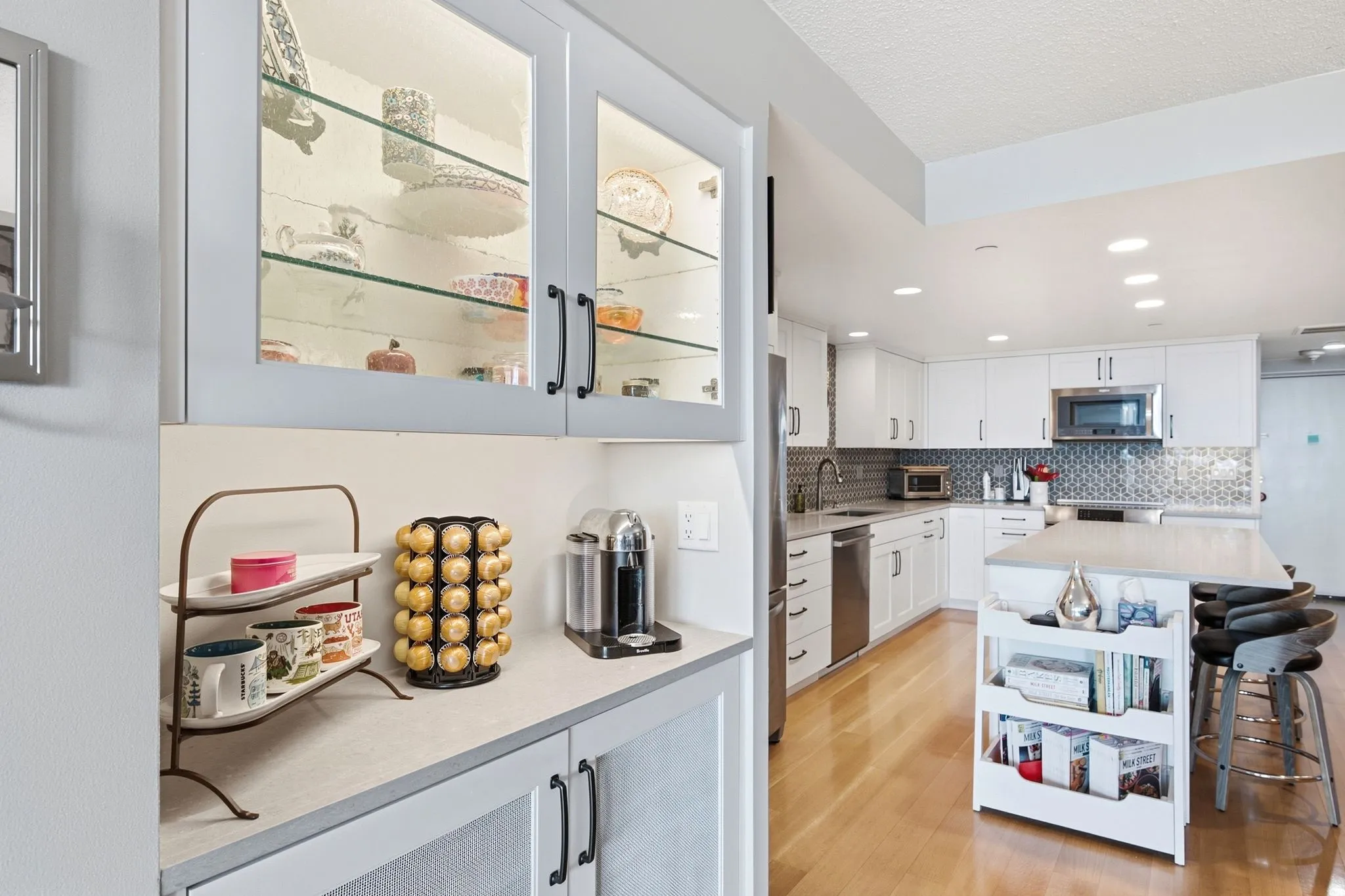 Modern kitchen featuring white cabinetry, stainless steel appliances, a mosaic tile backsplash, light wood-finish flooring, and a central island with seating