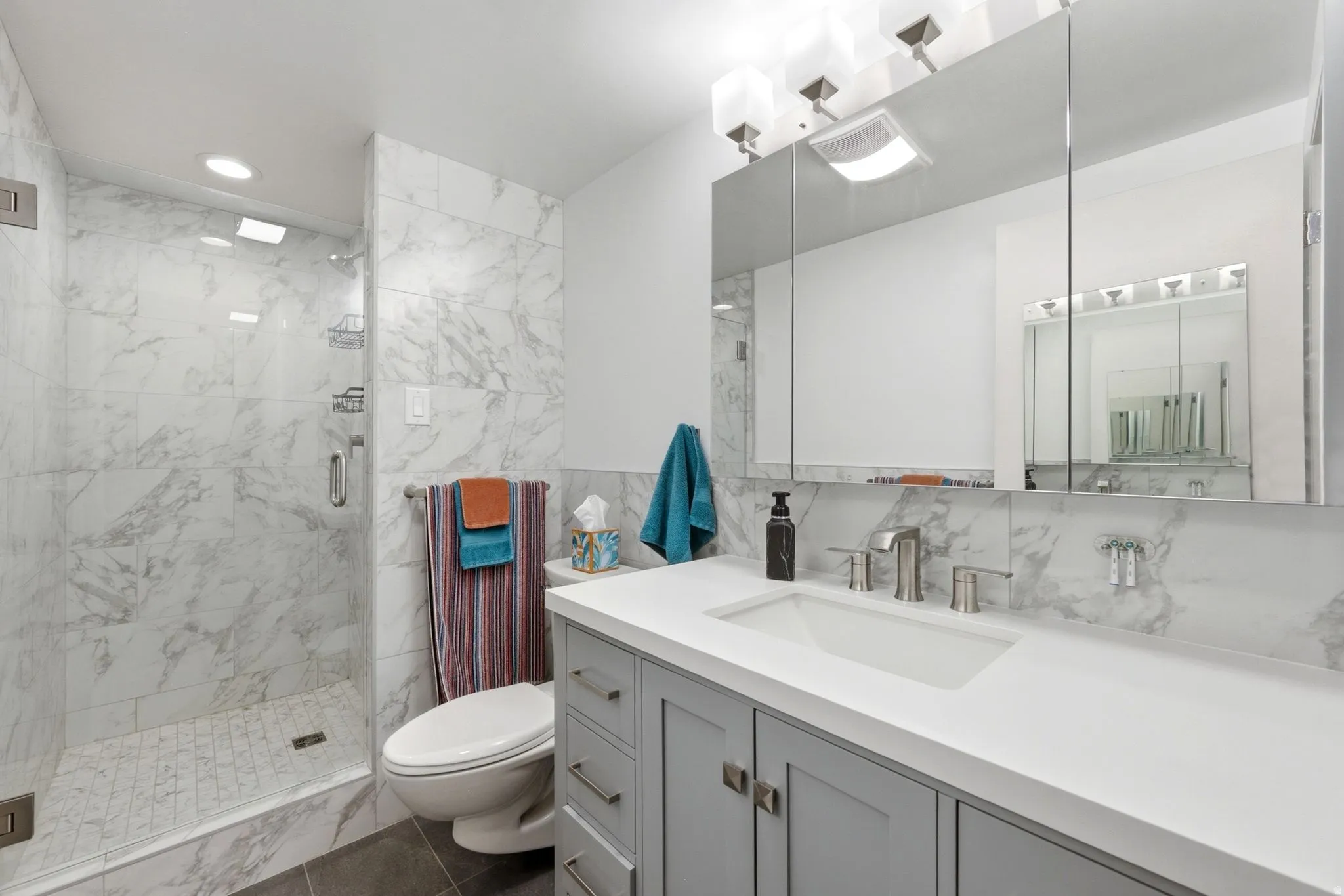Modern bathroom featuring a glass-enclosed shower with white marble-patterned tile, a matching marble-patterned backsplash, a white rectangular undermount sink, a wide vanity with gray shaker-style cabinetry, and brushed nickel fixtures