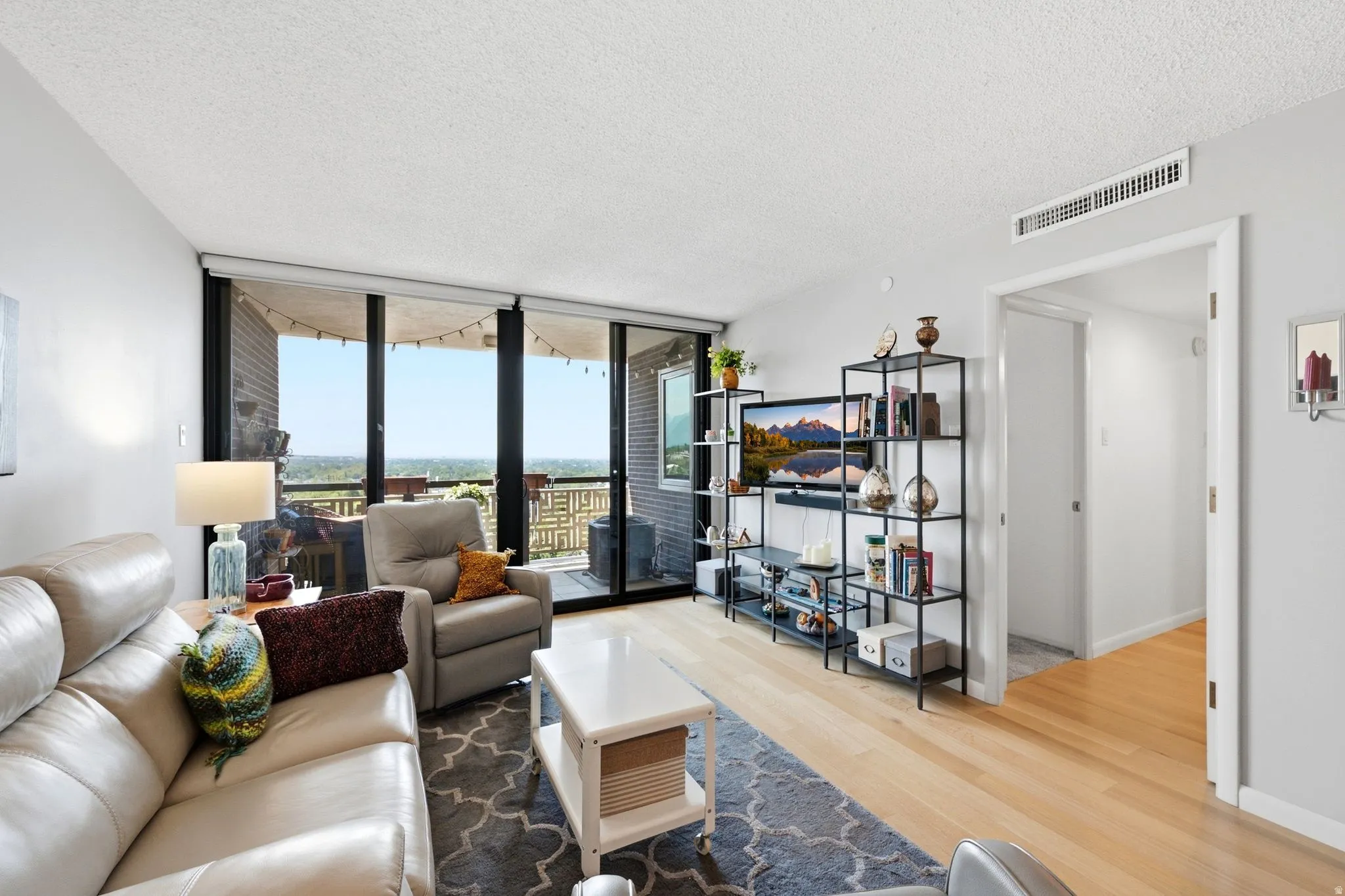 Living room featuring floor-to-ceiling windows, light wood-finish flooring, white walls, and a private balcony