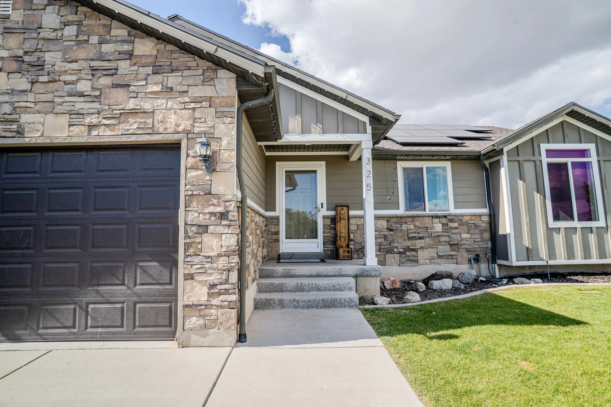 Stone veneer facade featuring a dark paneled garage door and an inviting front entry