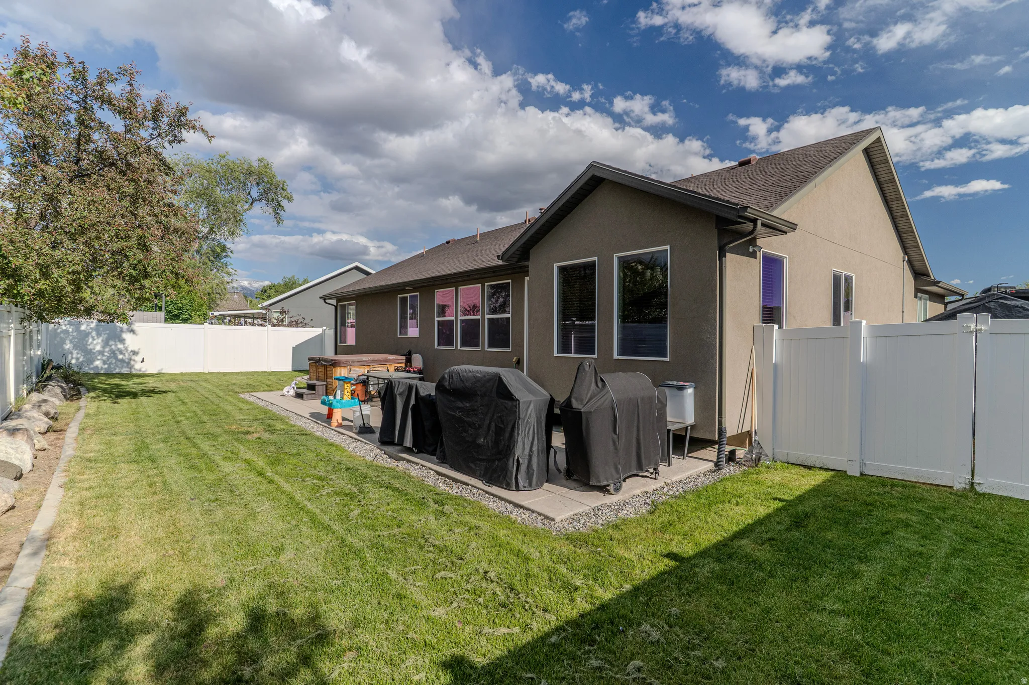 Spacious backyard featuring a large green lawn, a white privacy fence, and mature trees