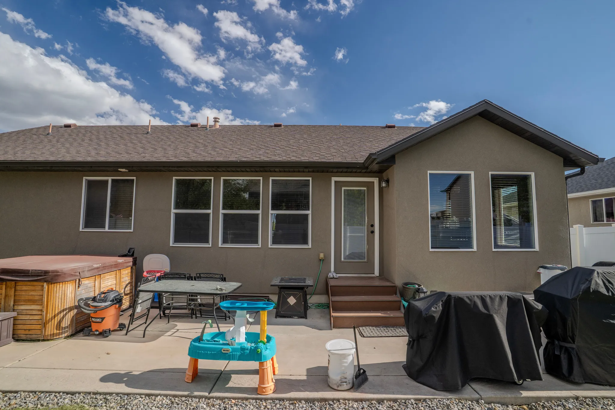 Rear exterior with a concrete patio, wooden hot tub, two-tier wooden steps, and multiple windows