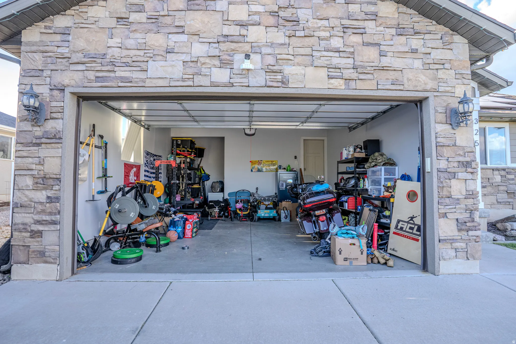 Two-car garage featuring a concrete floor, light stone exterior, two exterior sconces, and a side window