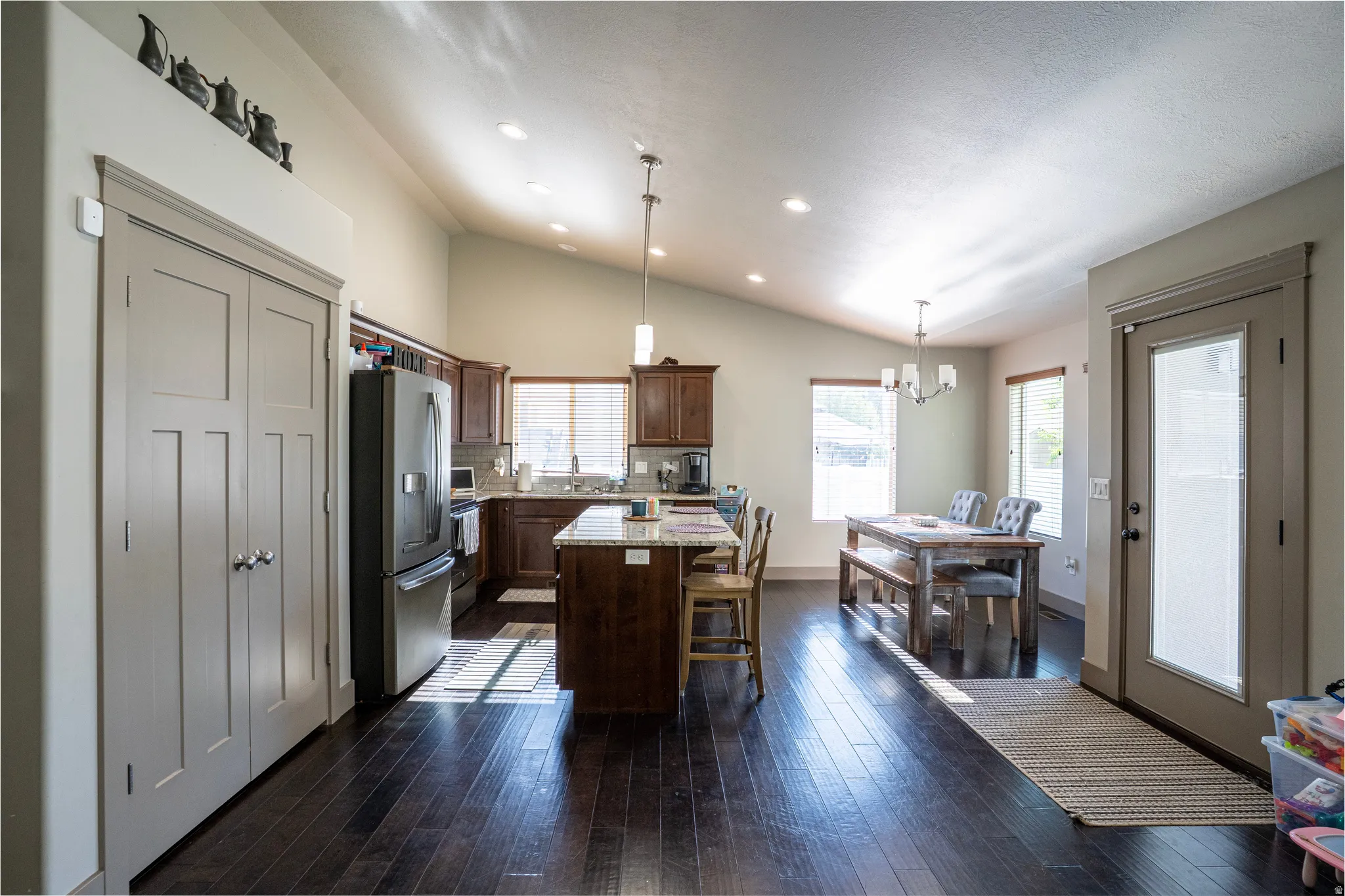 Open-concept living space featuring wood-finish flooring, vaulted ceilings, recessed lighting, and a kitchen island with stone countertop