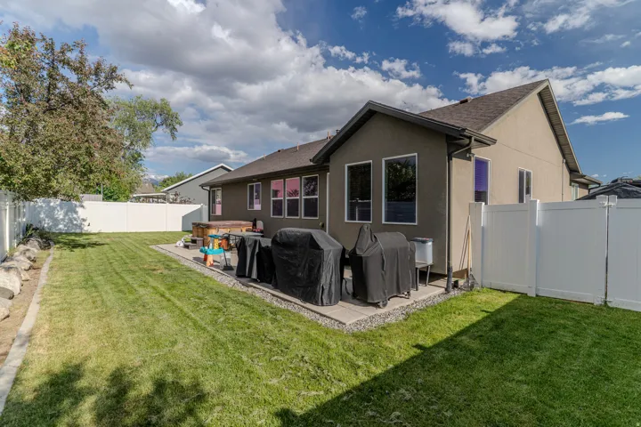 Spacious backyard featuring a large green lawn, a white privacy fence, and mature trees