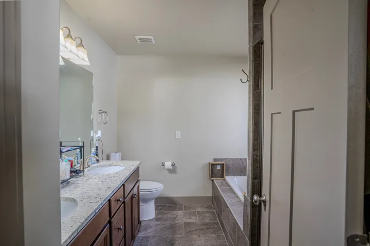 Double vanity with undermount sinks and light-toned countertop, wood-finish cabinetry, a drop-in tub with tile surround, and large format tile flooring