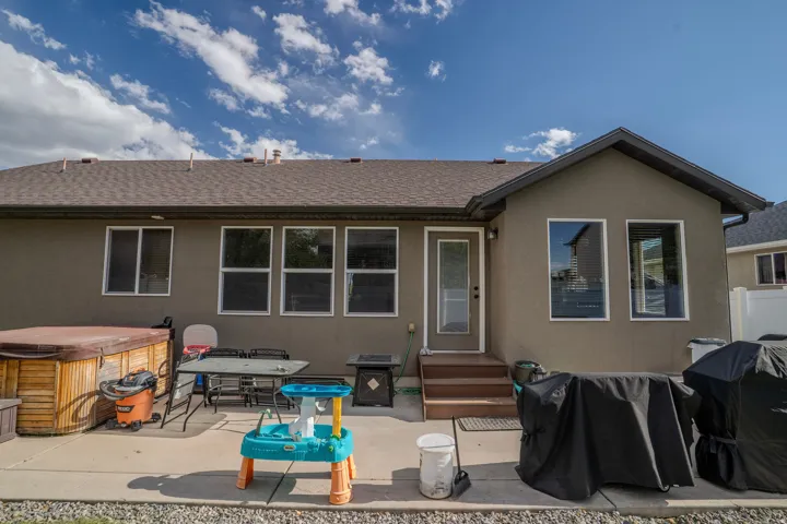 Rear exterior with a concrete patio, wooden hot tub, two-tier wooden steps, and multiple windows