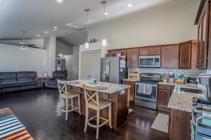 Open concept kitchen featuring granite countertops, wood-finish flooring, stainless steel appliances, a subway tile backsplash, and recessed lighting