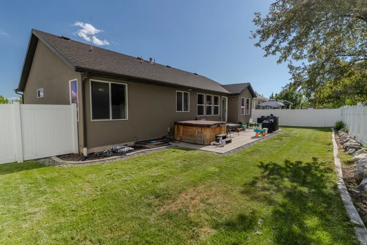 Expansive backyard featuring a rectangular lawn, concrete patio, perimeter vinyl fencing, and a built-in hot tub