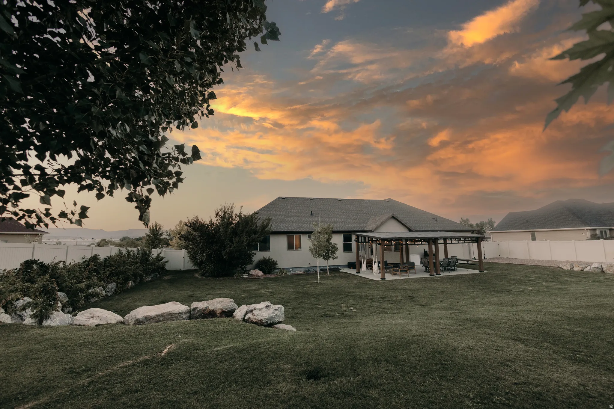 Expansive backyard featuring a large lawn, a paved patio with a pergola, and established perimeter landscaping