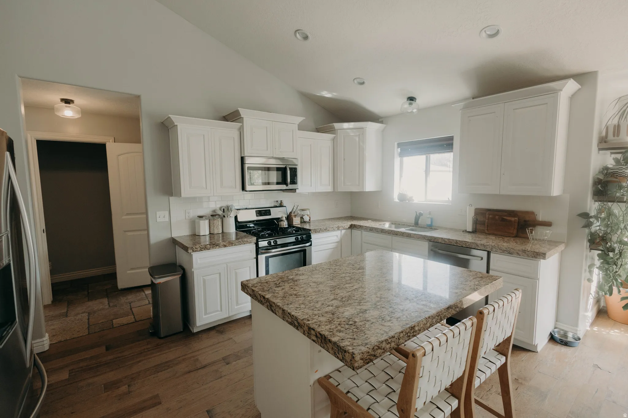 Kitchen featuring white cabinetry, granite countertops, stainless steel appliances, wood-finish flooring, and a central island