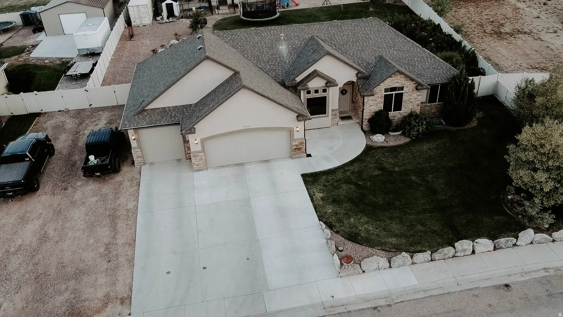 Stucco and stone exterior featuring a two-car garage, concrete driveway, and a landscaped lawn with mature trees