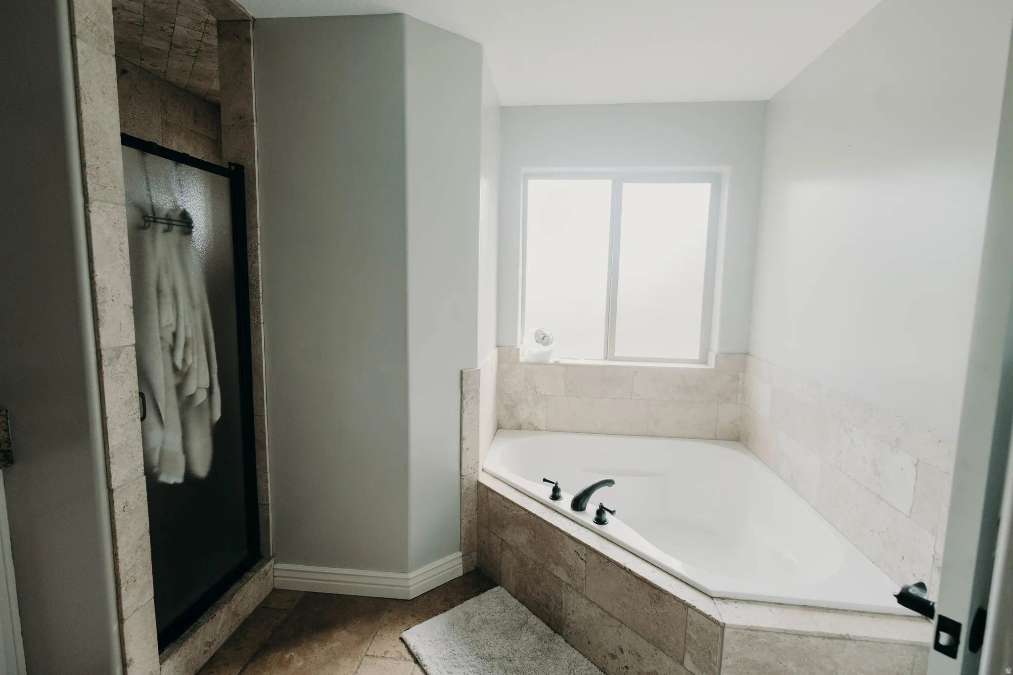 Corner soaking tub with dark-finish fixtures and frosted window