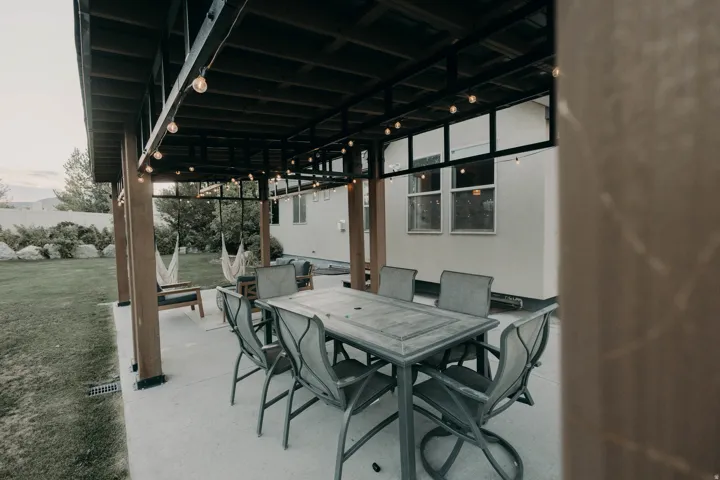 Covered patio featuring string lighting and multiple seating areas, alongside a manicured lawn
