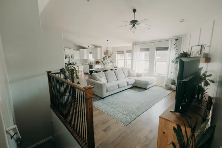 Open-concept living space featuring wood-finish flooring, a contemporary ceiling fan, and multiple windows with blinds