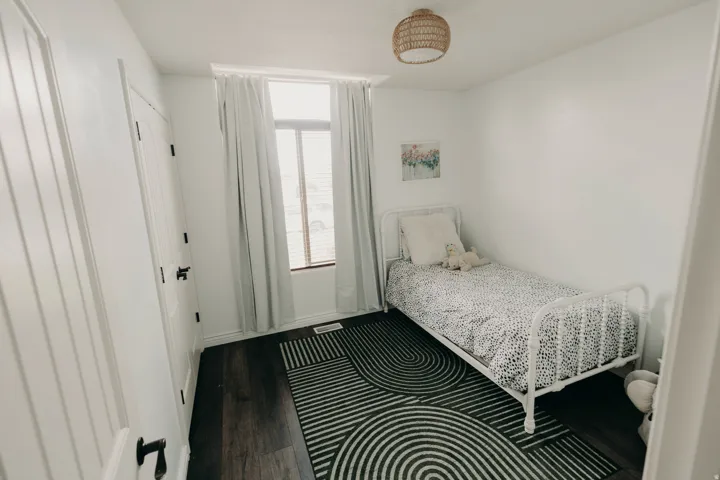 Bright room with dark wood-finish flooring, white walls, and a single window with blinds