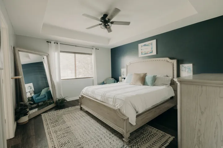 Recessed tray ceiling with ceiling fan, wood-finish flooring, and natural light from a window with blinds