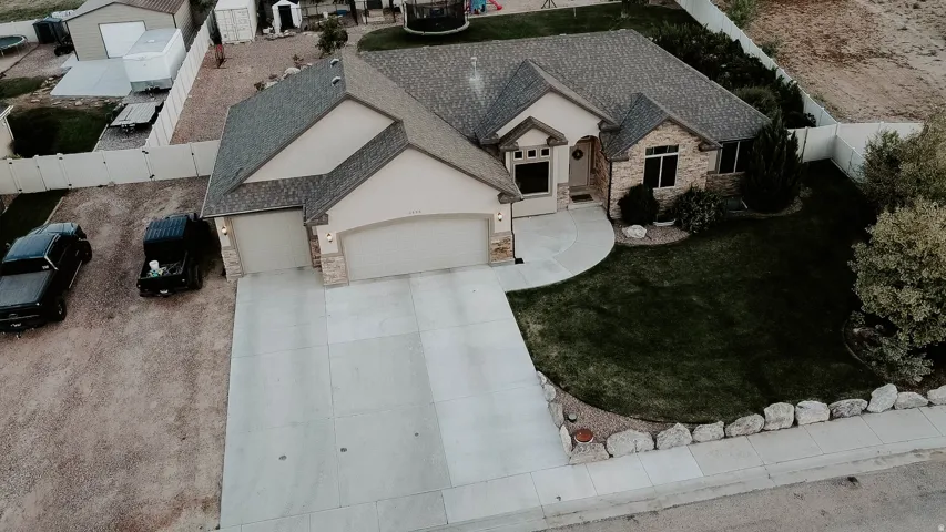 Stucco and stone exterior featuring a two-car garage, concrete driveway, and a landscaped lawn with mature trees