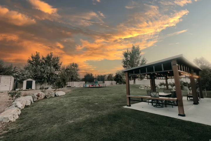 Spacious backyard featuring a built-in pergola with a solid roof, a concrete patio, a large manicured lawn, and a decorative rock border