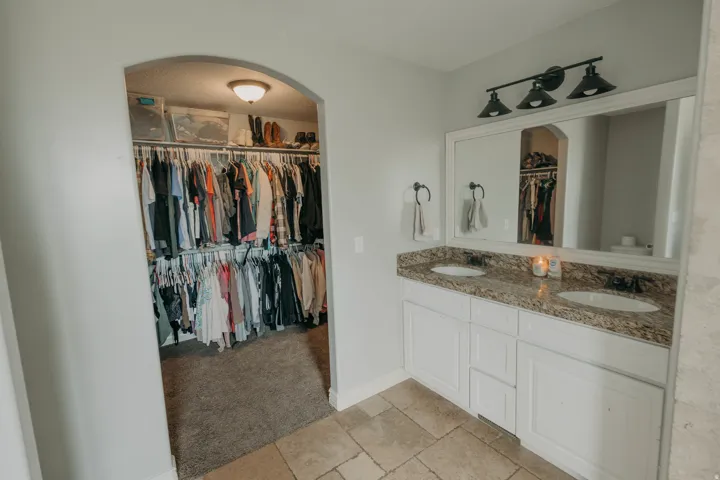 Bathroom vanity featuring dual undermount sinks, granite-finish countertop, and white cabinetry with brushed nickel hardware