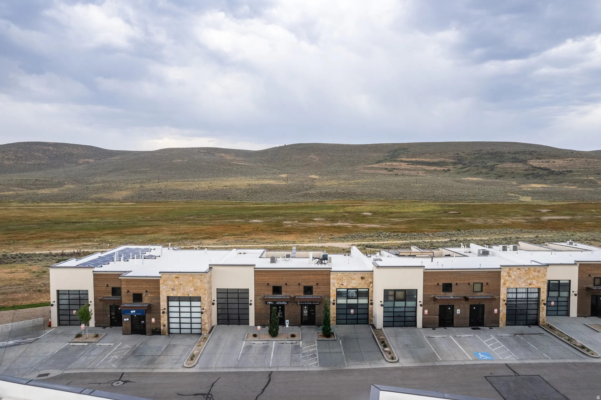 Contemporary multi-unit structure featuring a flat roof with solar panels, stone and wood-tone exterior accents, glass-paneled overhead doors, and individual entryways
