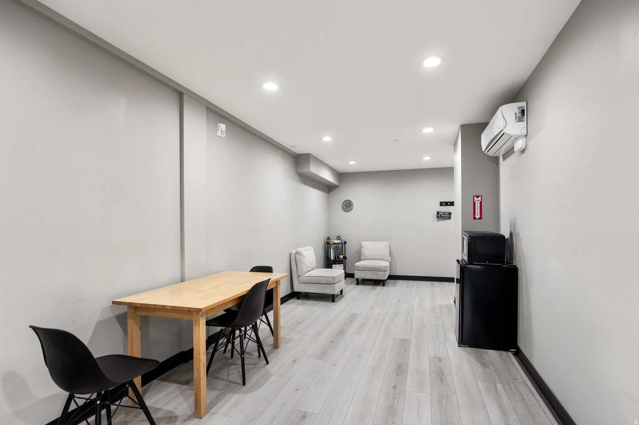 Spacious room featuring light wood-finish flooring, recessed lighting, and a wall-mounted air conditioning unit