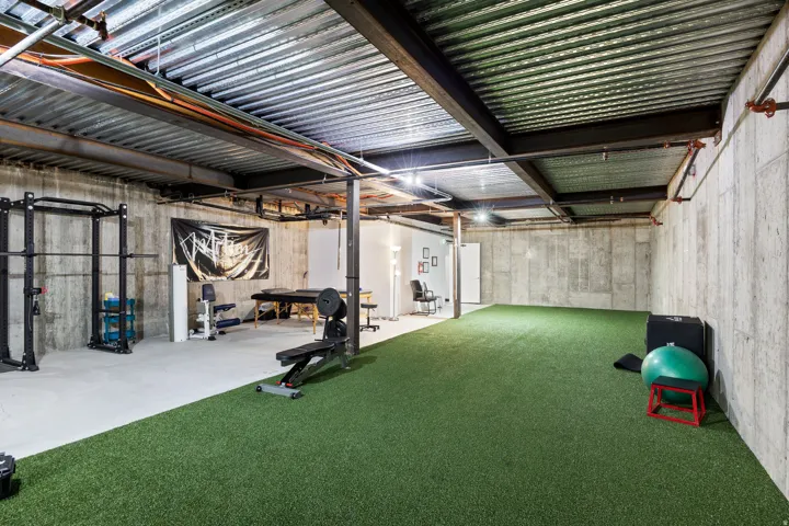 Spacious open area featuring a green turf floor section, exposed structural ceiling, concrete walls, and recessed lighting