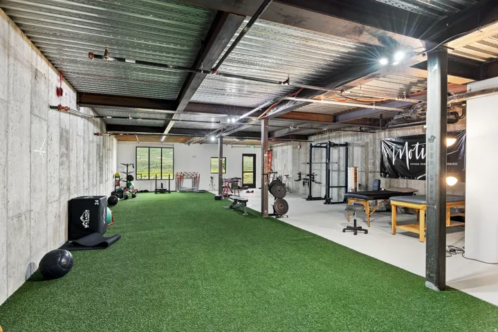 Spacious multi-purpose room featuring a concrete foundation, exposed structural beams, and a combination of artificial turf and concrete flooring