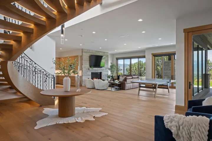 Curved wood staircase with wrought iron railing, light wood-finish flooring, recessed lighting, stone fireplace, and large sliding glass doors