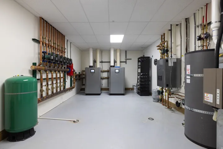 Dedicated utility room featuring comprehensive mechanical systems, including a pressurized expansion tank, multiple copper pipe manifolds, two water heaters, and a rack-mounted system