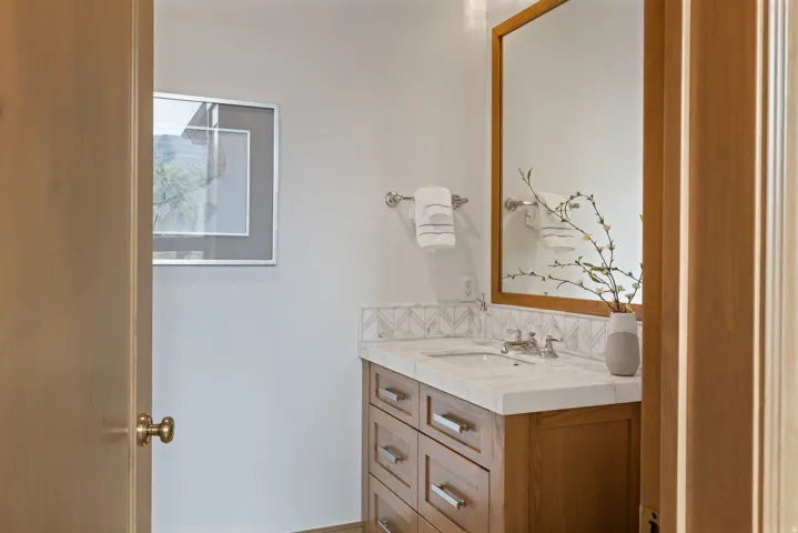Vanity featuring a light wood-finish cabinet with drawers, a stone countertop, a rectangular undermount sink, and a framed mirror