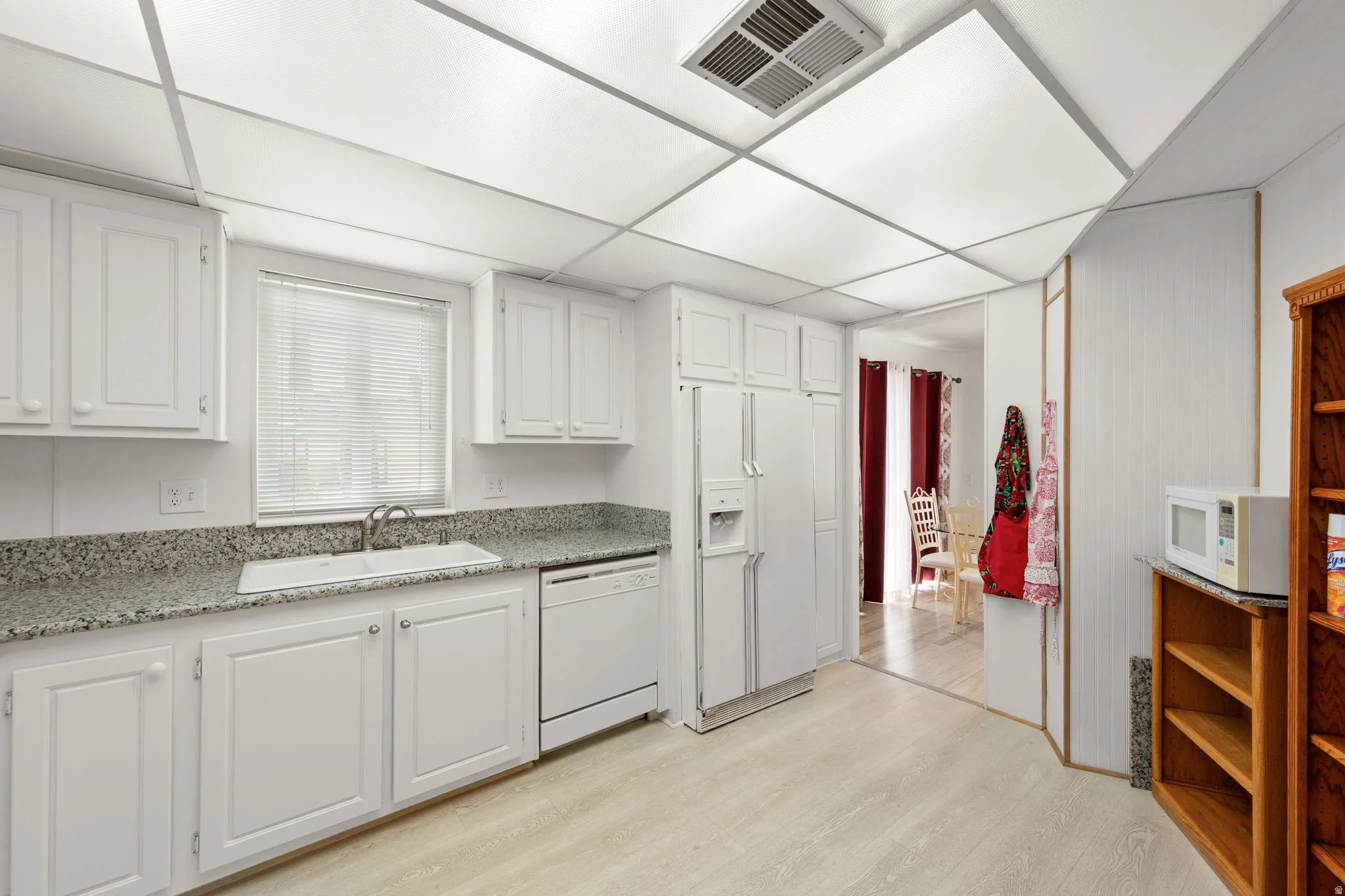 Kitchen featuring white cabinetry, light-toned wood-finish flooring, recessed lighting, a built-in dishwasher, and a window with blinds