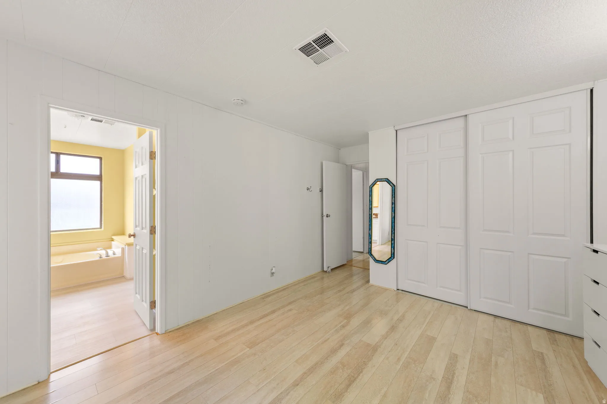 Bright room with light wood-finish flooring, white walls, and sliding panel closet doors