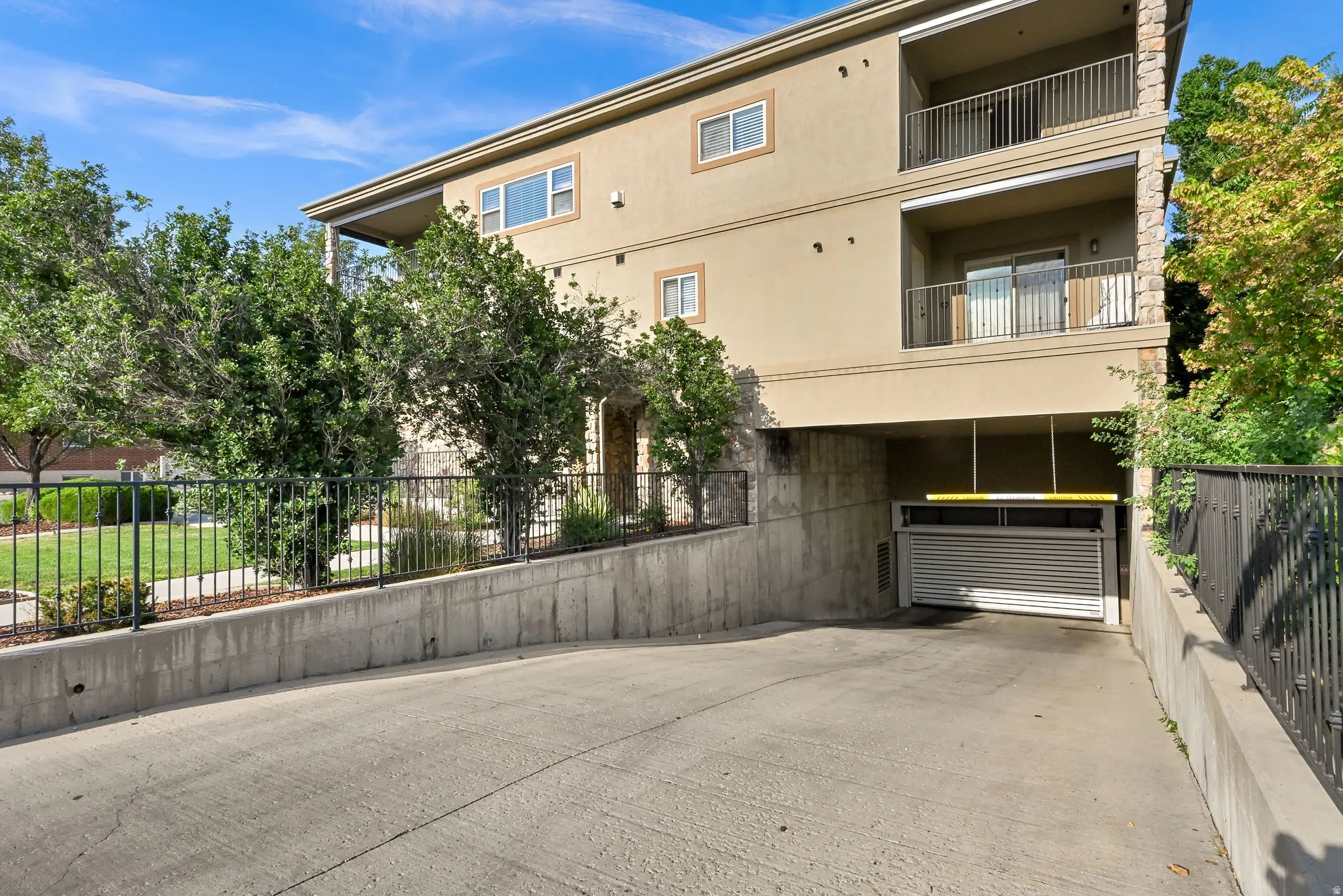 Underground Garage Entrance: Modern stucco exterior featuring multiple balconies with metal railings, a ground-level garage with a roll-up door, and a concrete driveway