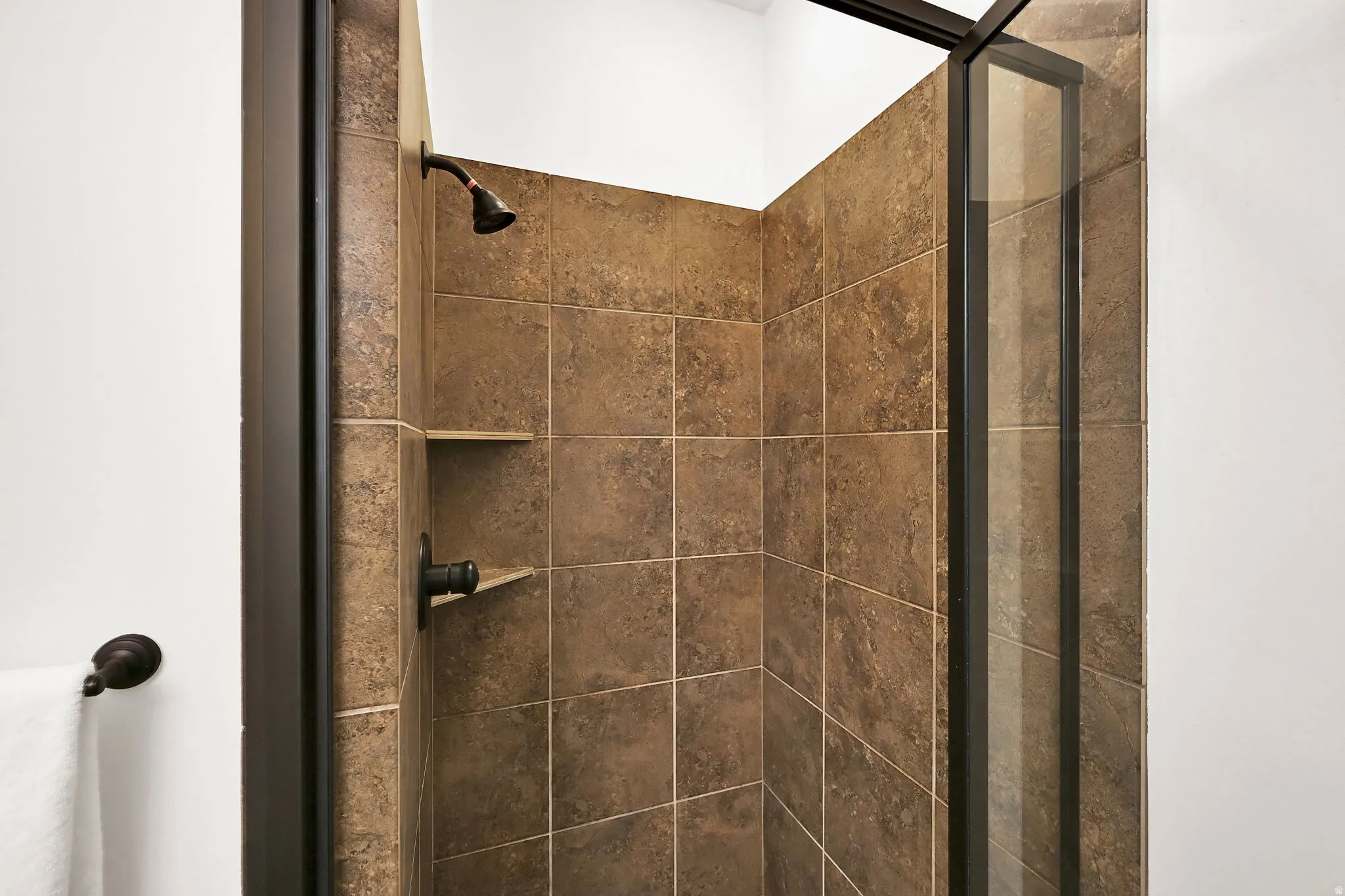 Shower enclosure featuring brown square-set wall tiles, a built-in shower niche, and oil-rubbed bronze fixtures