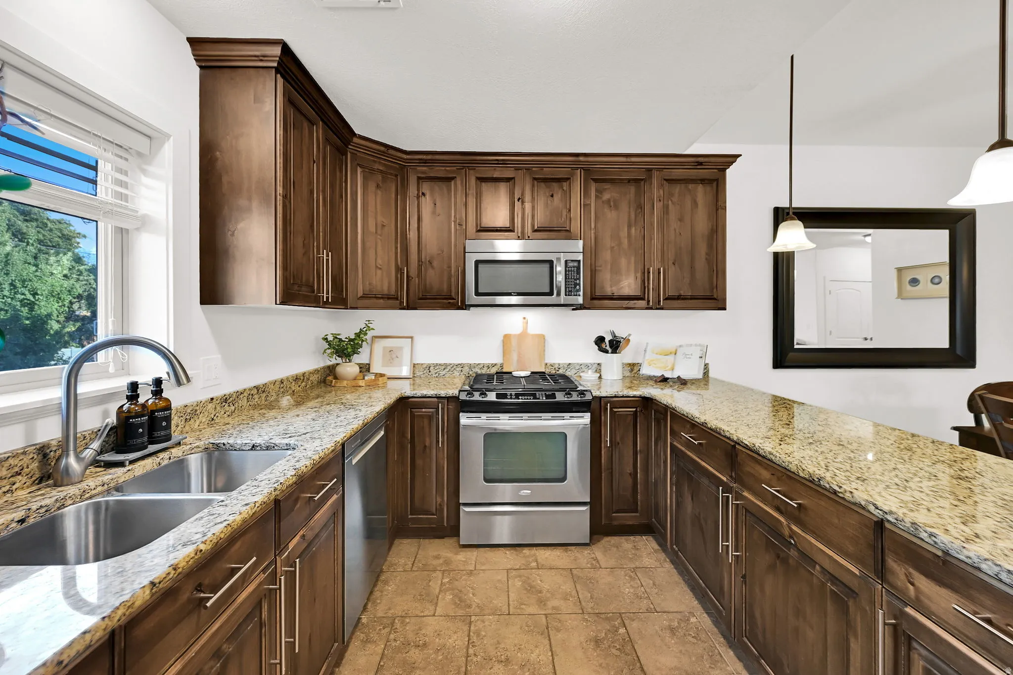 U-shaped kitchen featuring wood cabinetry, light-toned granite countertops, and stainless steel appliances