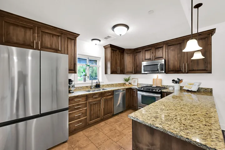 Kitchen featuring rich wood cabinetry with crown molding, new stainless steel refrigerator and dishwasher, granite countertops, and tile flooring