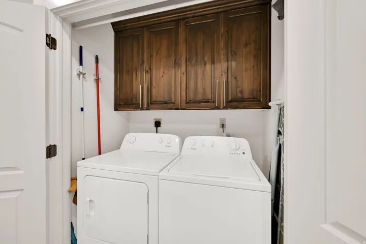 Laundry area featuring wood-finish cabinetry with brushed nickel hardware and white doors which enclose the washer and dryer