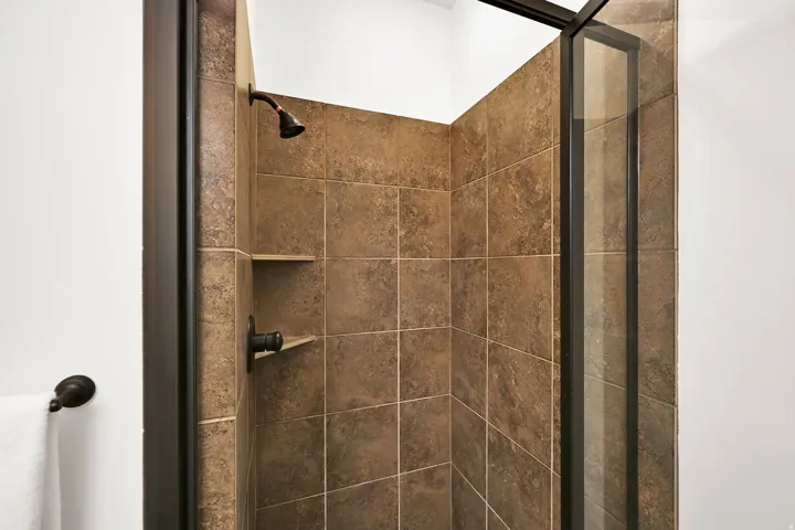Shower enclosure featuring brown square-set wall tiles, a built-in shower niche, and oil-rubbed bronze fixtures