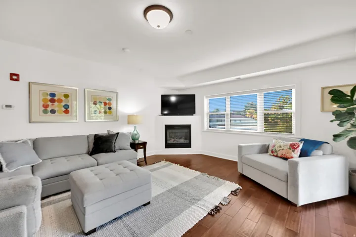 Living area featuring wood flooring, white walls, and a recessed corner fireplace with a mounted television