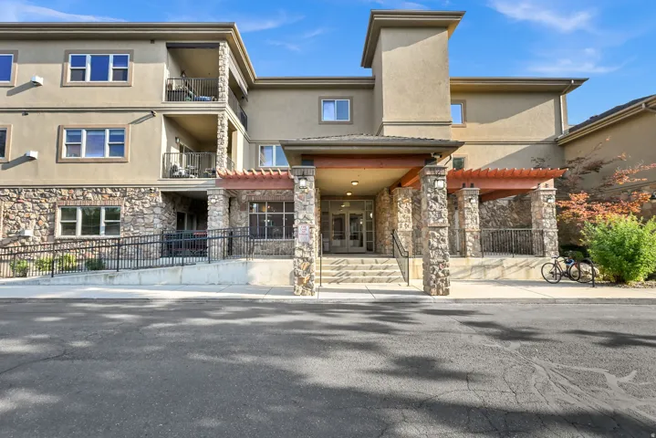 Main Entrance: Multistory building exterior featuring a prominent stone facade, multiple private balconies with metal railings, a covered entry with stone columns, and a concrete ramp with metal handrails
