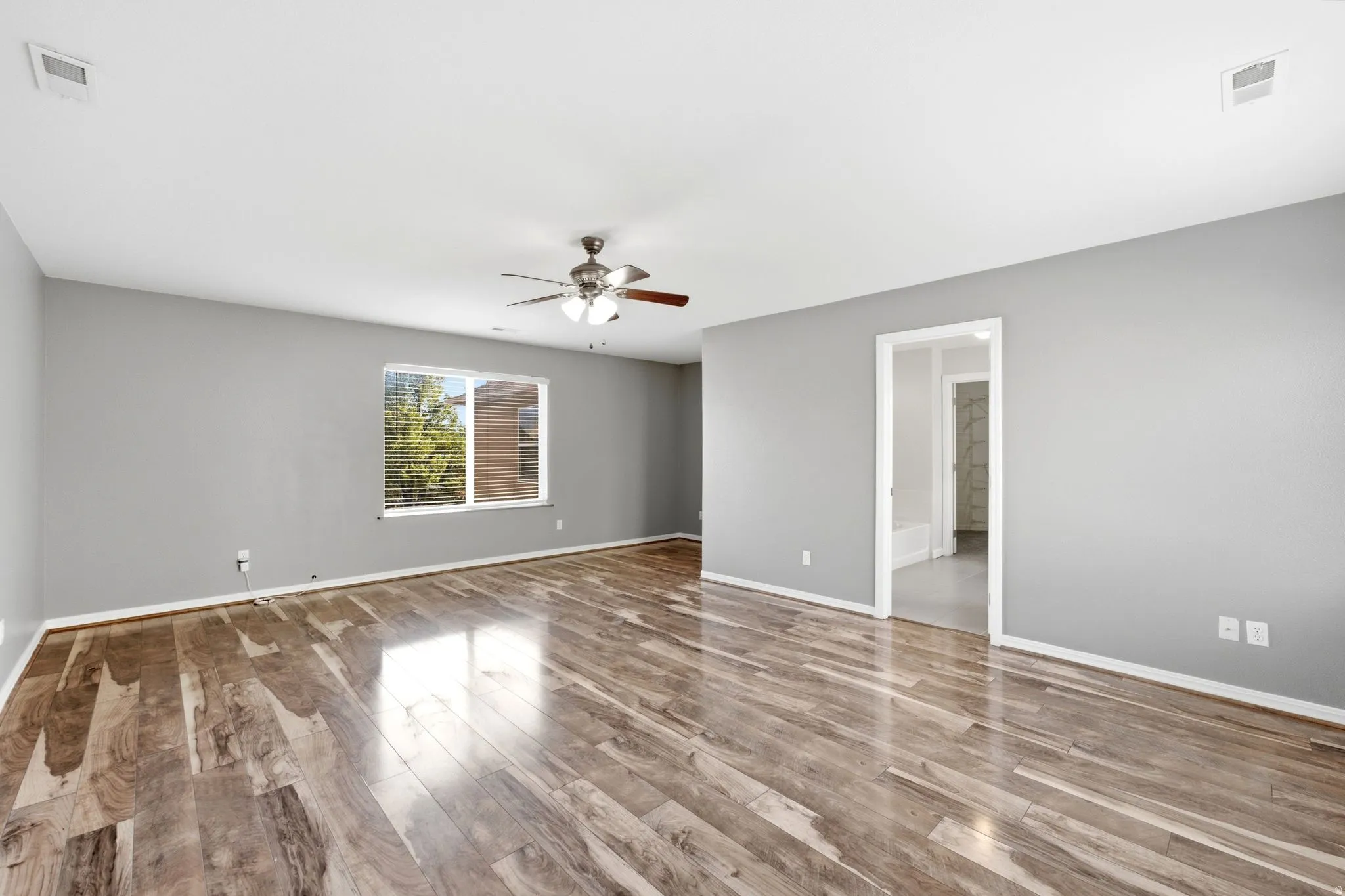 Spacious room featuring wood-finish flooring, a window with horizontal blinds, a ceiling fan, and light gray wall finishes