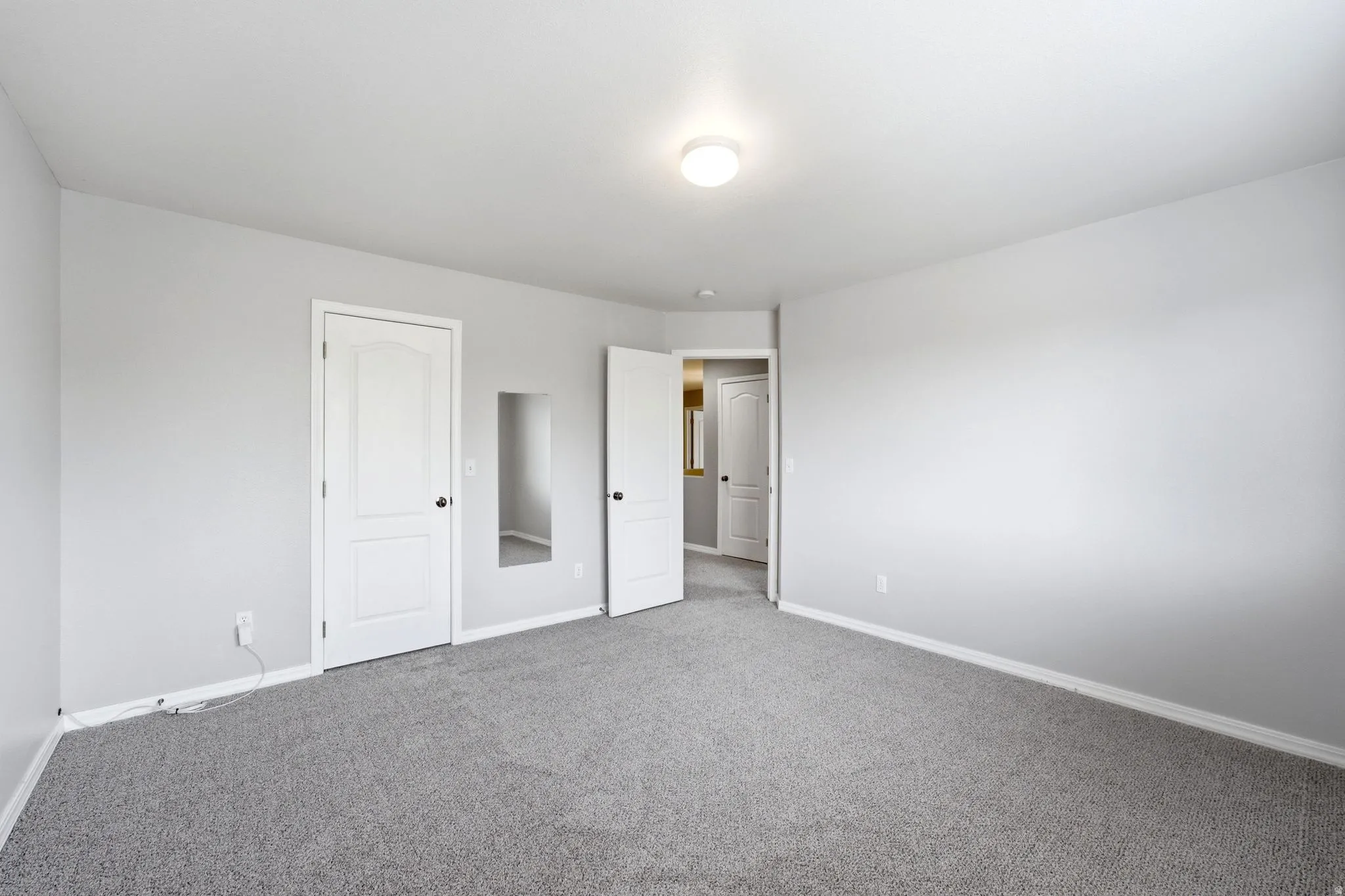 Carpeted room featuring light gray wall paint, a flush-mount ceiling light fixture, white baseboards, and white interior doors with black hardware