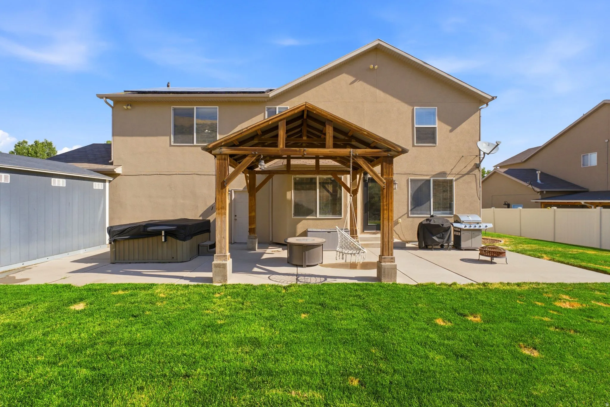 Expansive backyard featuring a manicured lawn, a large concrete patio, and a dedicated wooden gazebo structure