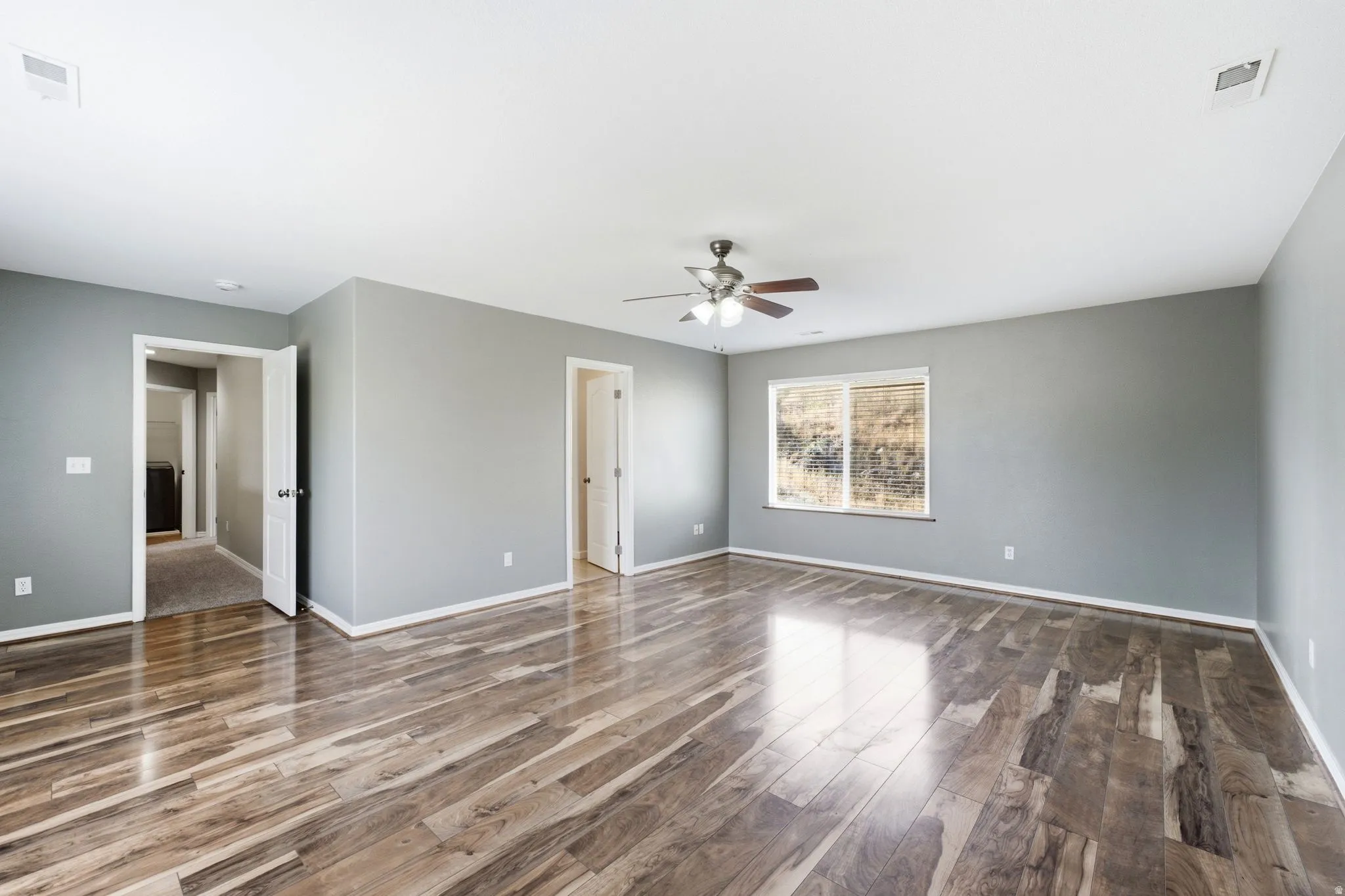 Spacious room featuring wood-finish flooring, light gray walls, white trim, and a ceiling fan with integrated lighting