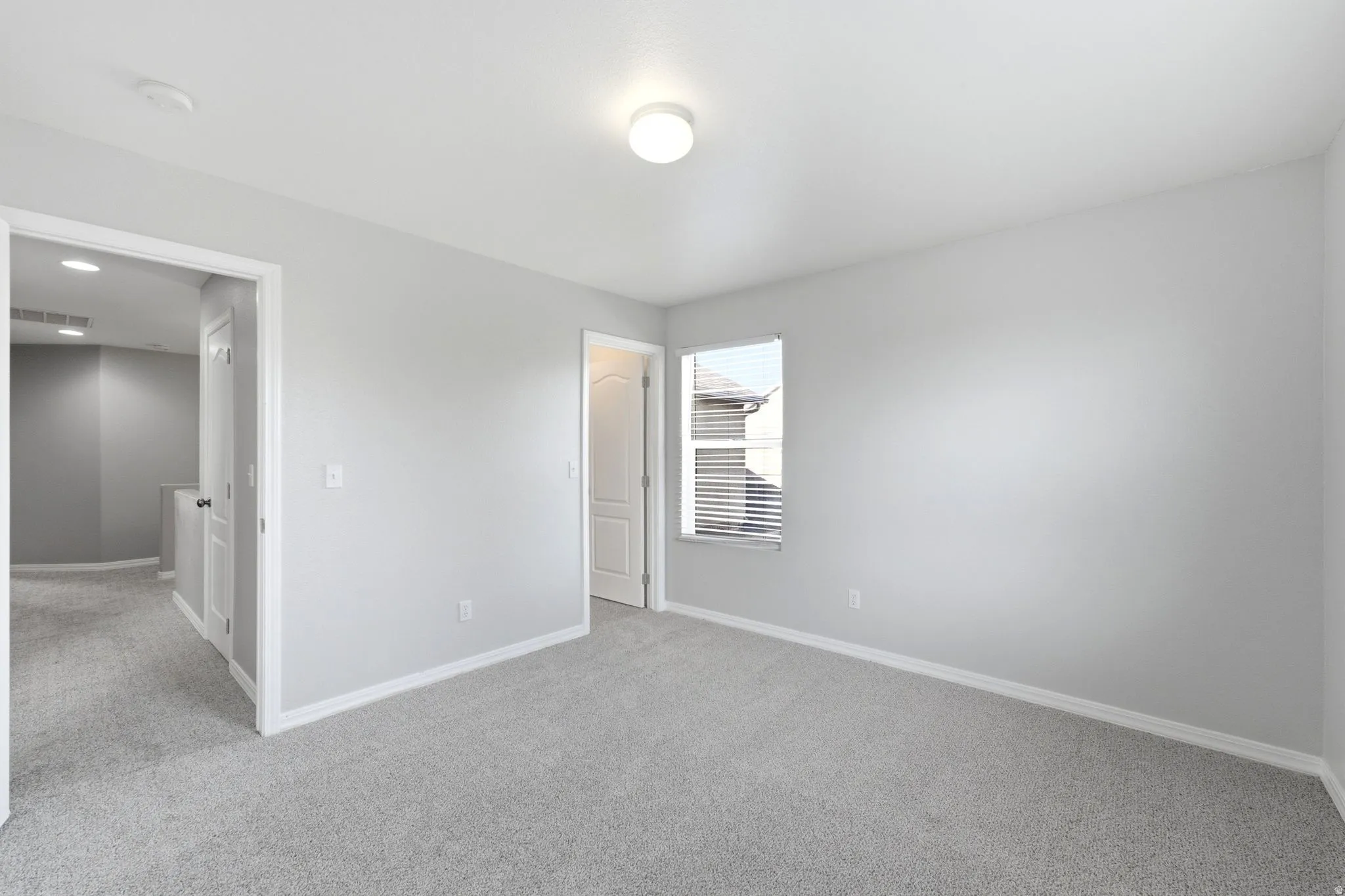 Spacious room featuring light gray carpeting, neutral wall paint, white trim, and a window with blinds